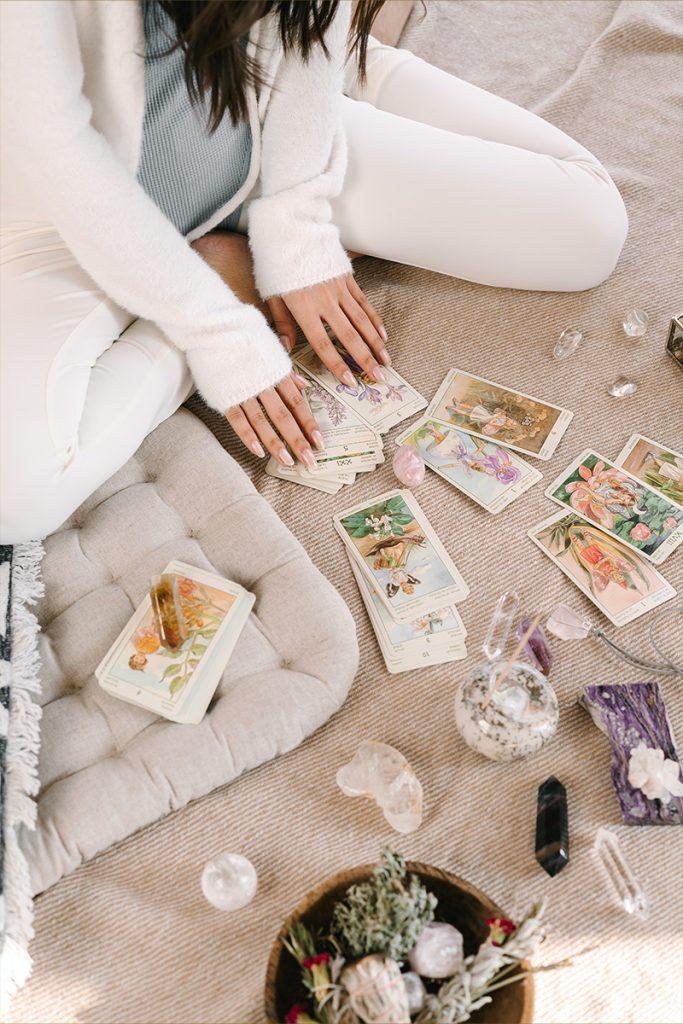 She carefully sets up her sacred space, laying out a beautiful silk cloth to protect her cards. She begins by wiping down each card with a soft, dry cloth to remove any dust or smudges that may have accumulated since her last reading. As she works, she takes care to handle each card gently and with reverence.